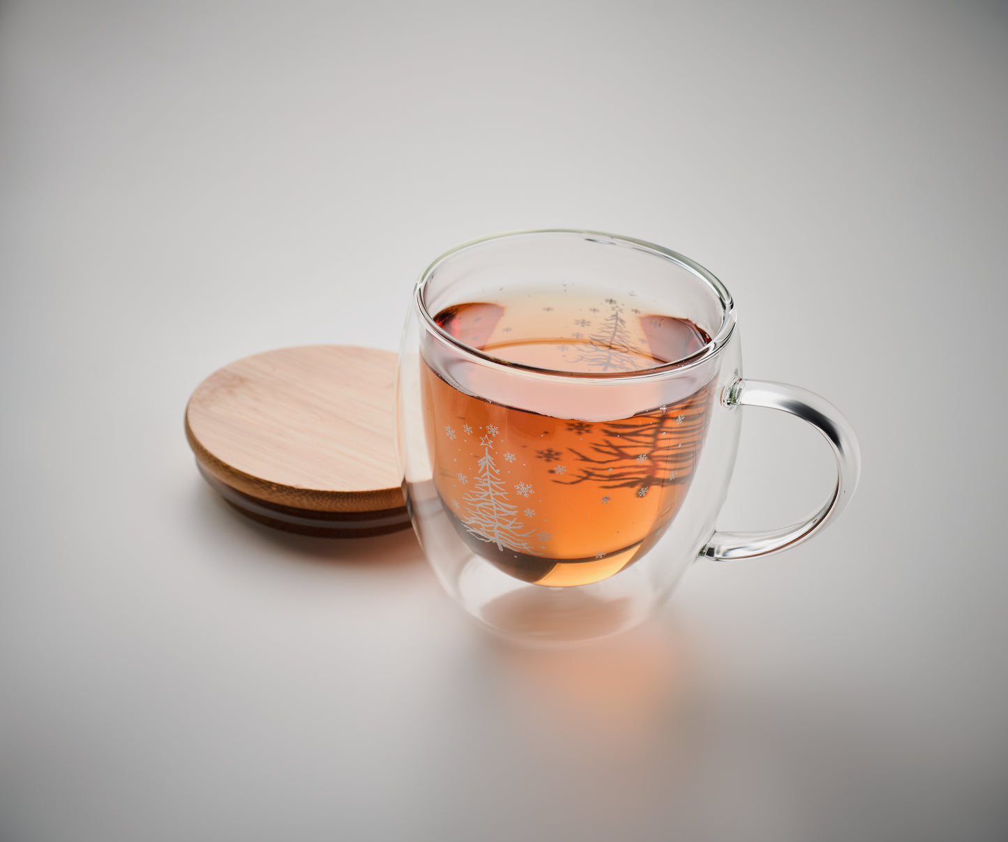 Doppelwandiger Becher mit Weihnachtsbaum-Dekor aus Borosilikatglas. Deckel aus Bambus. Füllmenge: 220 ml.
