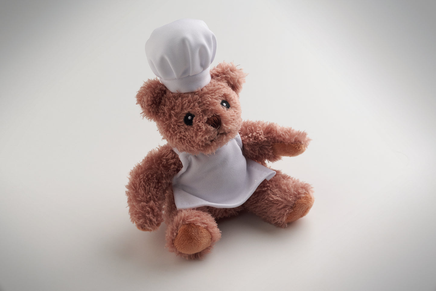 Teddybär aus Polyester gekleidet als Koch mit weißer Kochmütze und Schürze. Augen