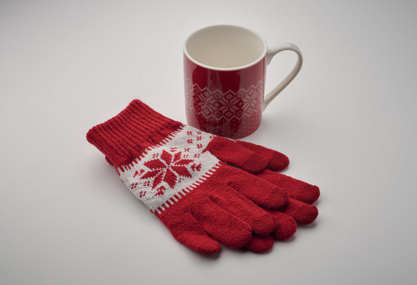 Winterliches Geschenkset bestehend aus einem Paar gestrickter taktiler Handschuhe und Keramikbecher. Schneeflockenmuster.