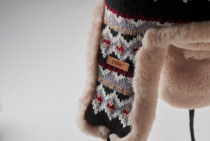 Gestrickte Mütze mit Ohrenklappen und Bommel aus Acrylfaser mit Polyester- und Fleece-Futter.